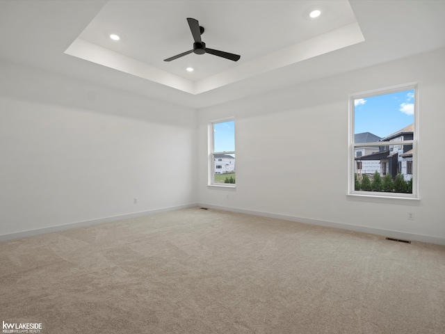 carpeted spare room with a raised ceiling and ceiling fan