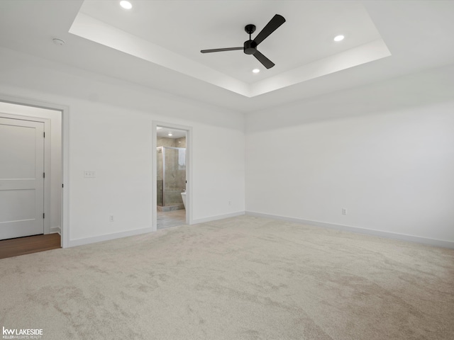 carpeted spare room featuring a tray ceiling and ceiling fan