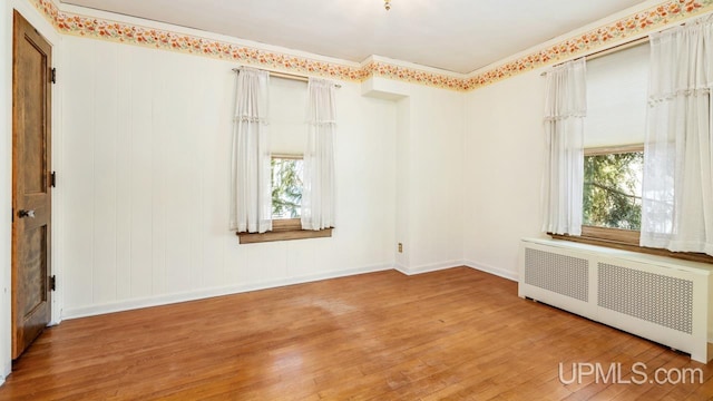 spare room featuring hardwood / wood-style flooring, radiator heating unit, ornamental molding, and a wealth of natural light