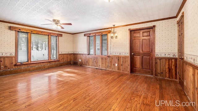 unfurnished room with wood walls, wood-type flooring, ceiling fan, crown molding, and a textured ceiling