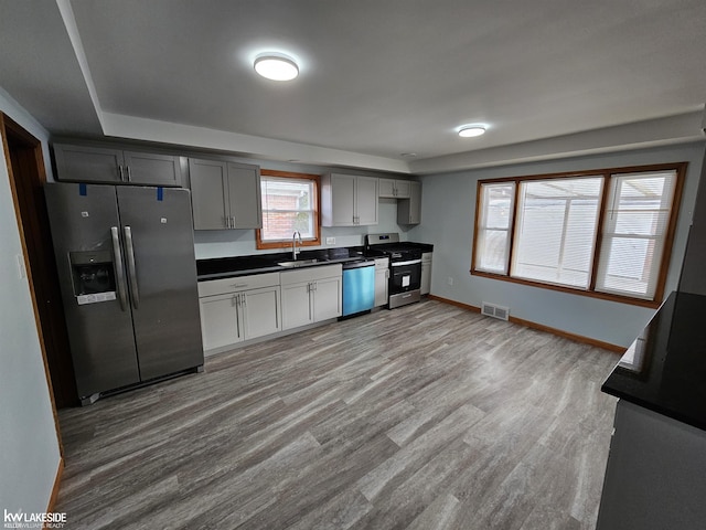 kitchen with light wood-type flooring, stainless steel appliances, sink, and gray cabinetry