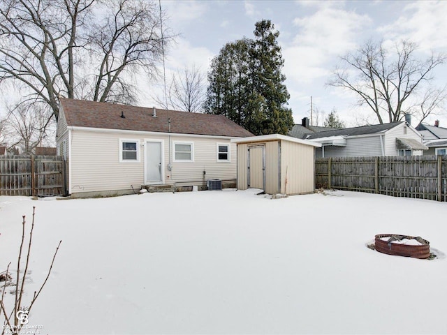 snow covered rear of property featuring a storage shed, central air condition unit, and an outdoor fire pit