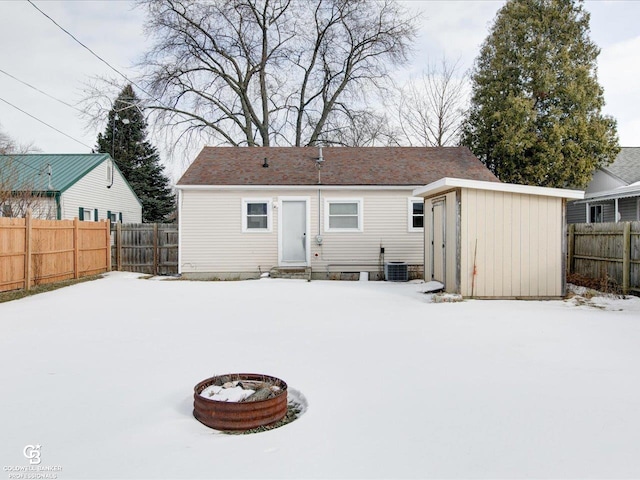 snow covered house with a fire pit, cooling unit, and a storage shed