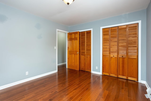 unfurnished bedroom with two closets and dark wood-type flooring