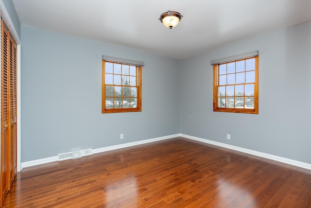 unfurnished bedroom featuring multiple windows, dark hardwood / wood-style flooring, and a closet