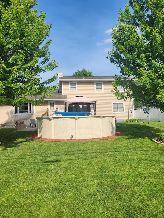 rear view of property featuring an empty pool, a gazebo, and a lawn