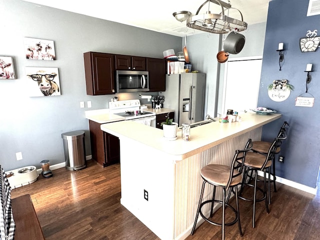 kitchen featuring dark wood-type flooring, a breakfast bar, stainless steel appliances, dark brown cabinetry, and kitchen peninsula