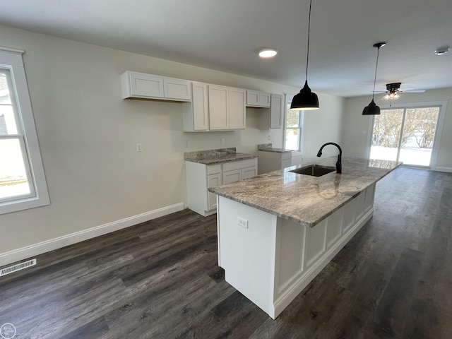 kitchen featuring sink, light stone counters, an island with sink, white cabinets, and decorative light fixtures