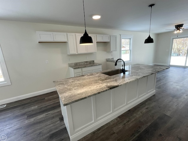 kitchen featuring pendant lighting, white cabinetry, sink, light stone countertops, and a center island with sink