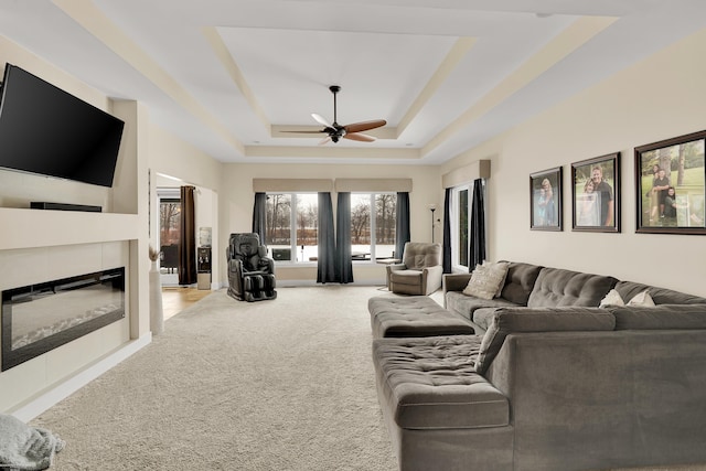 carpeted living room with a fireplace, a raised ceiling, and ceiling fan