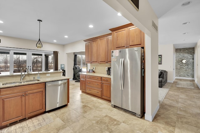 kitchen featuring sink, appliances with stainless steel finishes, tasteful backsplash, light stone countertops, and decorative light fixtures