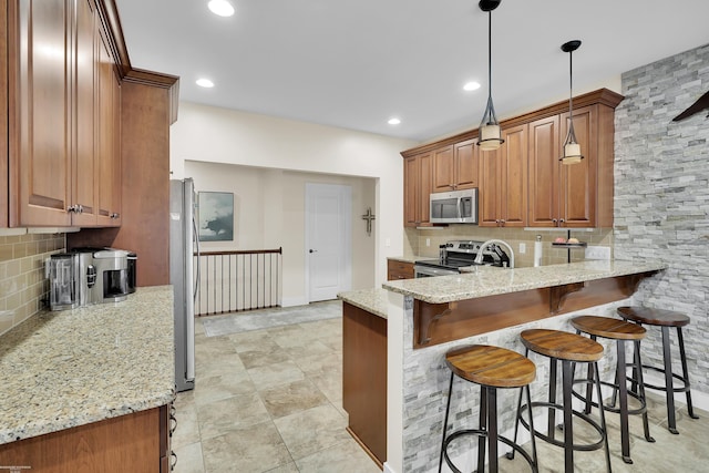 kitchen featuring a breakfast bar, appliances with stainless steel finishes, light stone countertops, decorative light fixtures, and kitchen peninsula