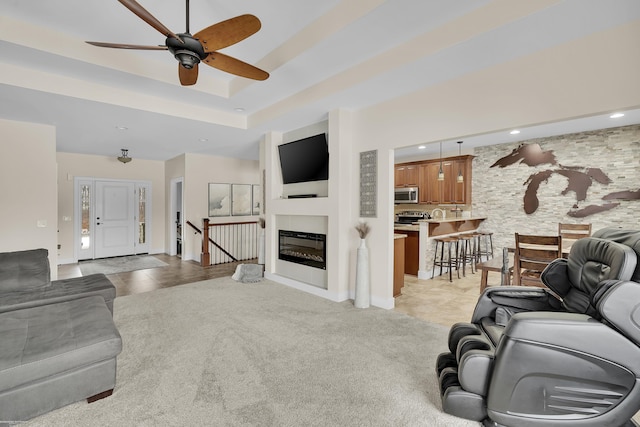 carpeted living room featuring a raised ceiling and ceiling fan