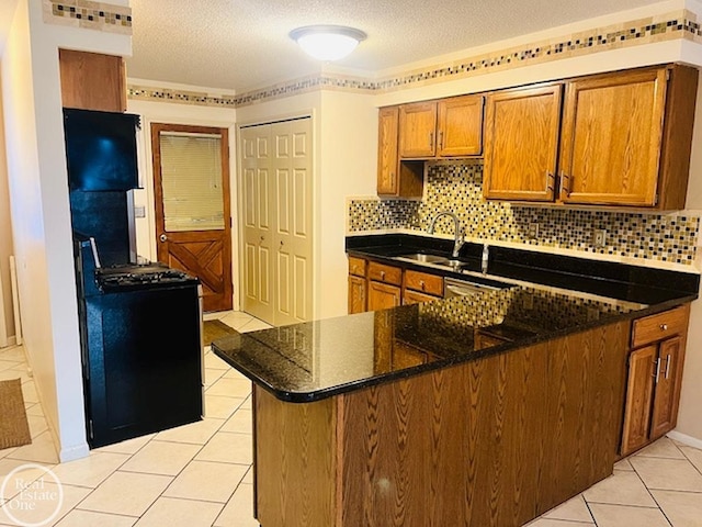 kitchen with light tile patterned flooring, sink, dark stone counters, kitchen peninsula, and gas range oven