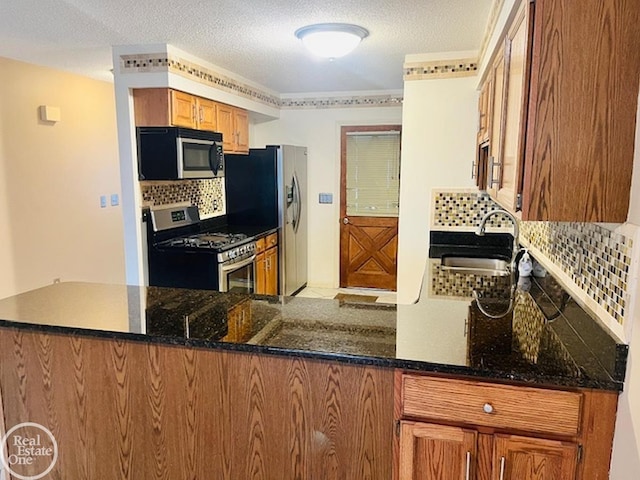 kitchen with sink, tasteful backsplash, dark stone counters, kitchen peninsula, and stainless steel appliances