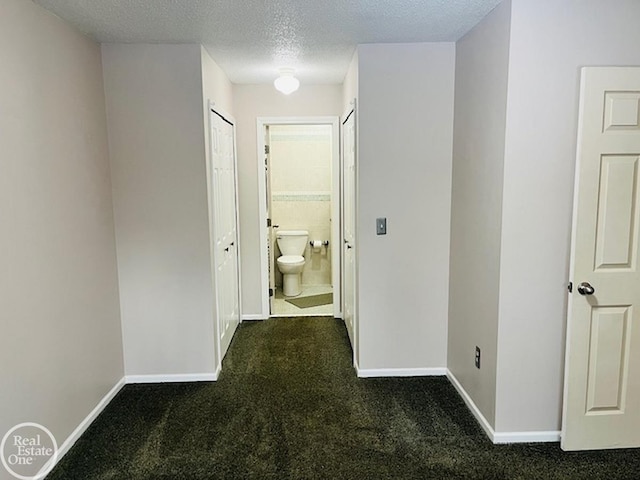 corridor with a textured ceiling and dark colored carpet