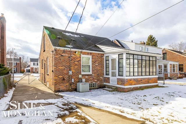 snow covered property featuring central AC and a sunroom