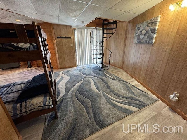 bedroom with wood-type flooring, a drop ceiling, and wood walls