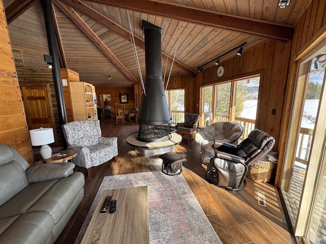 living room with plenty of natural light, wooden walls, lofted ceiling with beams, and a wood stove