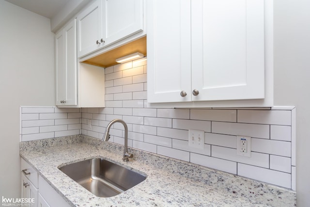 kitchen with white cabinetry, sink, light stone counters, and decorative backsplash