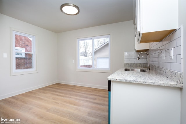 kitchen with sink, tasteful backsplash, light hardwood / wood-style flooring, light stone countertops, and white cabinets