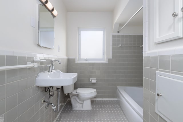 bathroom with tile walls, tile patterned floors, washtub / shower combination, and toilet