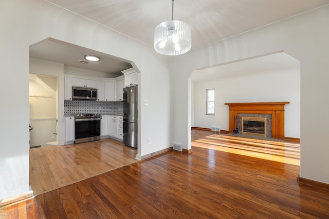 kitchen with white cabinetry, decorative light fixtures, appliances with stainless steel finishes, hardwood / wood-style flooring, and backsplash