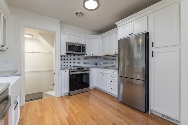 kitchen featuring stainless steel appliances, white cabinetry, backsplash, and light wood-type flooring