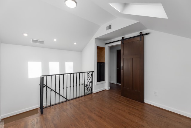 additional living space with dark wood-type flooring, a barn door, and vaulted ceiling