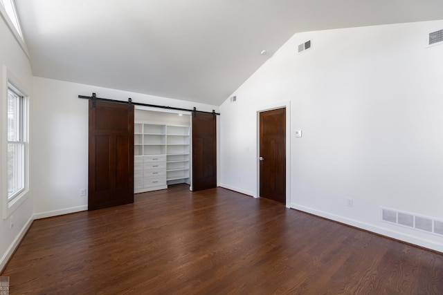 unfurnished bedroom with a barn door, high vaulted ceiling, and dark hardwood / wood-style flooring