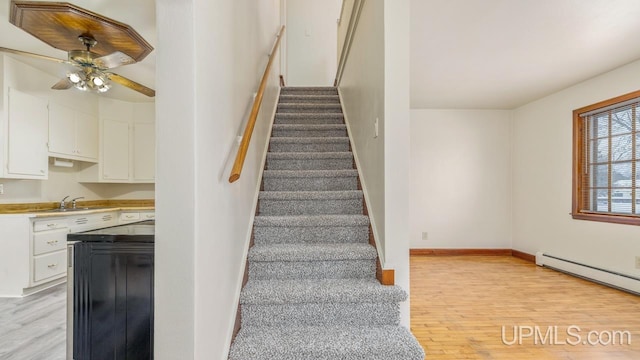 staircase with baseboard heating, ceiling fan, sink, and hardwood / wood-style floors