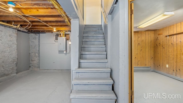 staircase featuring wood walls, concrete floors, and electric panel