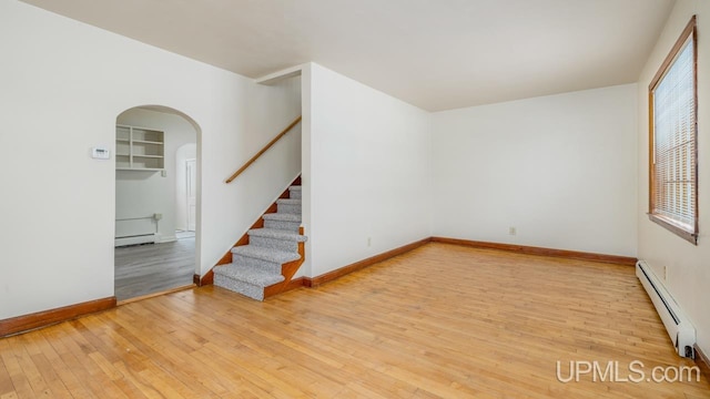 empty room with baseboard heating and light hardwood / wood-style flooring