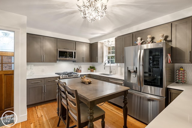 kitchen with sink, light hardwood / wood-style flooring, stainless steel appliances, tasteful backsplash, and a notable chandelier