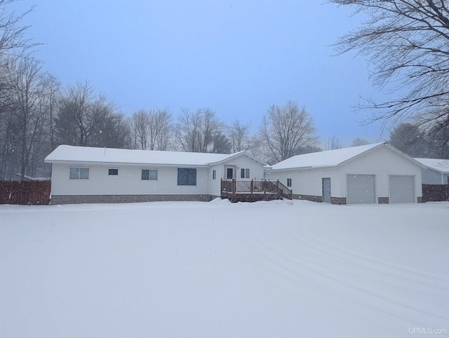 snow covered property with a garage, a wooden deck, and an outbuilding