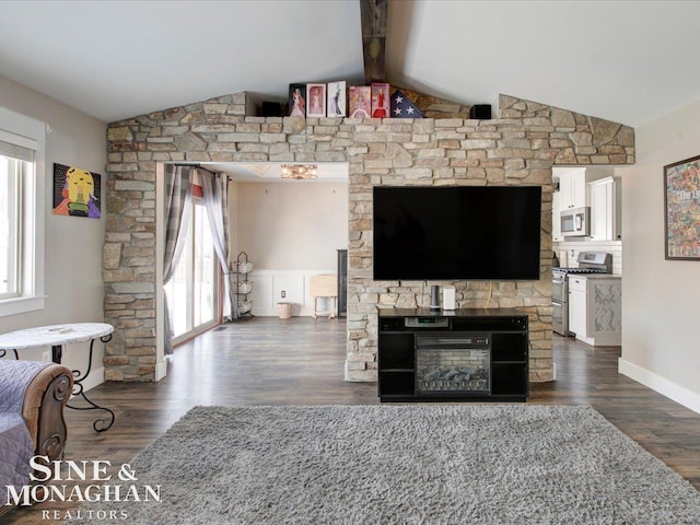 living room featuring a stone fireplace, a healthy amount of sunlight, vaulted ceiling with beams, and dark hardwood / wood-style floors