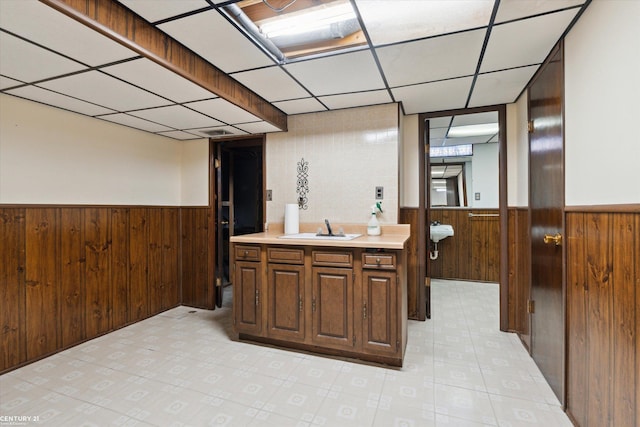 interior space with a drop ceiling, sink, and wood walls