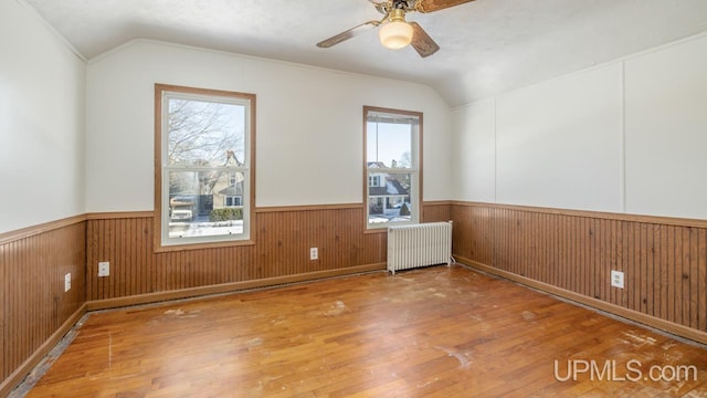 empty room with vaulted ceiling, radiator, hardwood / wood-style floors, wooden walls, and ceiling fan