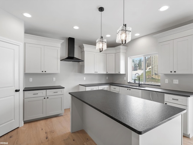 kitchen featuring pendant lighting, wall chimney range hood, sink, white cabinetry, and a kitchen island