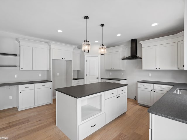 kitchen featuring wall chimney exhaust hood, light hardwood / wood-style flooring, hanging light fixtures, a kitchen island, and white cabinets