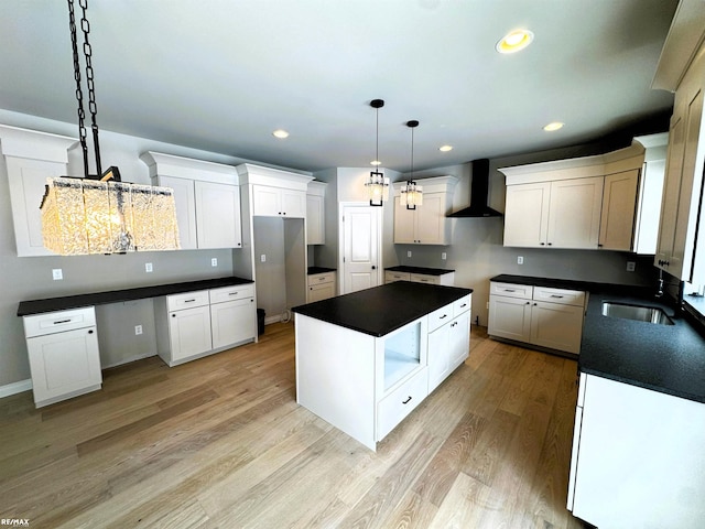 kitchen with wall chimney exhaust hood, sink, white cabinetry, decorative light fixtures, and a kitchen island