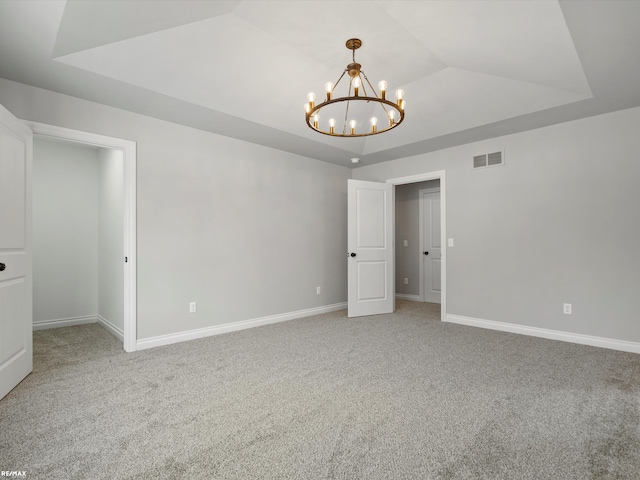 empty room featuring lofted ceiling, carpet flooring, a notable chandelier, and a tray ceiling