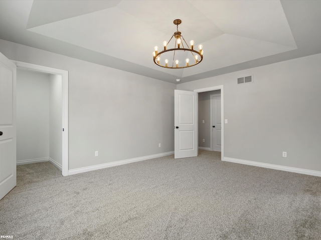 empty room with lofted ceiling, carpet floors, a notable chandelier, and a tray ceiling