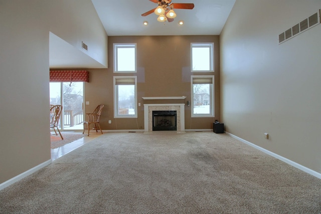 unfurnished living room with light colored carpet, ceiling fan, and a high ceiling