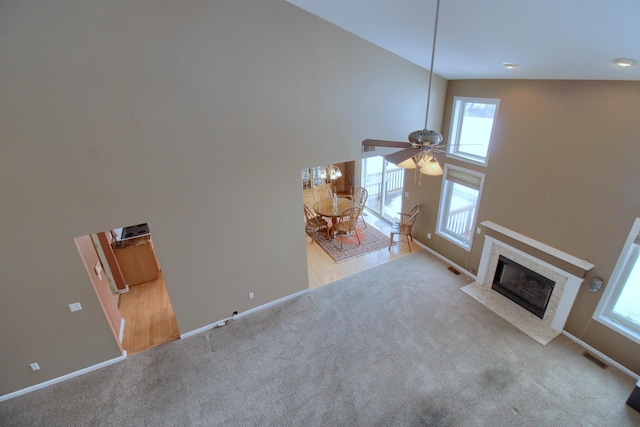 unfurnished living room with a high ceiling, a premium fireplace, light carpet, and ceiling fan