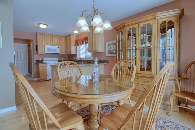 dining area with light wood-type flooring, sink, and an inviting chandelier