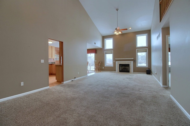 unfurnished living room featuring a high ceiling, light colored carpet, and ceiling fan