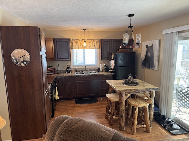 kitchen featuring pendant lighting, sink, hardwood / wood-style flooring, dark brown cabinetry, and black appliances