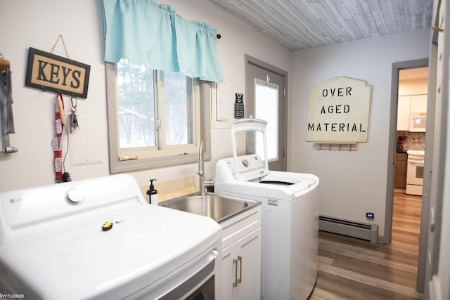 clothes washing area with sink, hardwood / wood-style flooring, washer and clothes dryer, cabinets, and a baseboard radiator