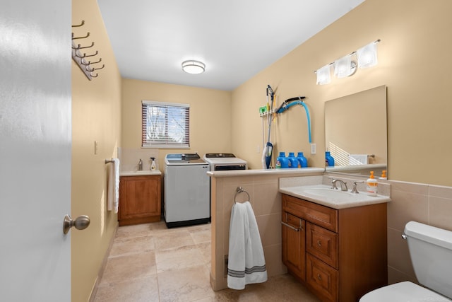 bathroom with washing machine and dryer, tile walls, vanity, and toilet